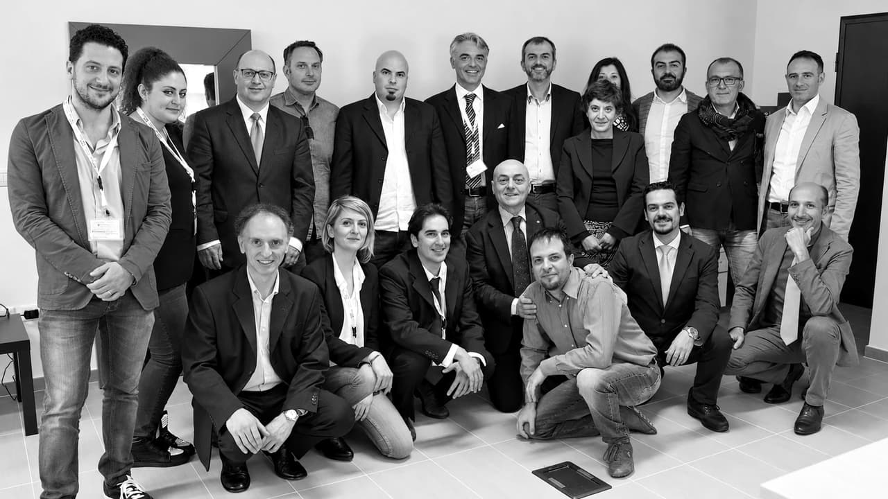 Giacomo Lenoci in una foto di gruppo con una ventina di persone, in piedi e accosciate, in un ufficio.
